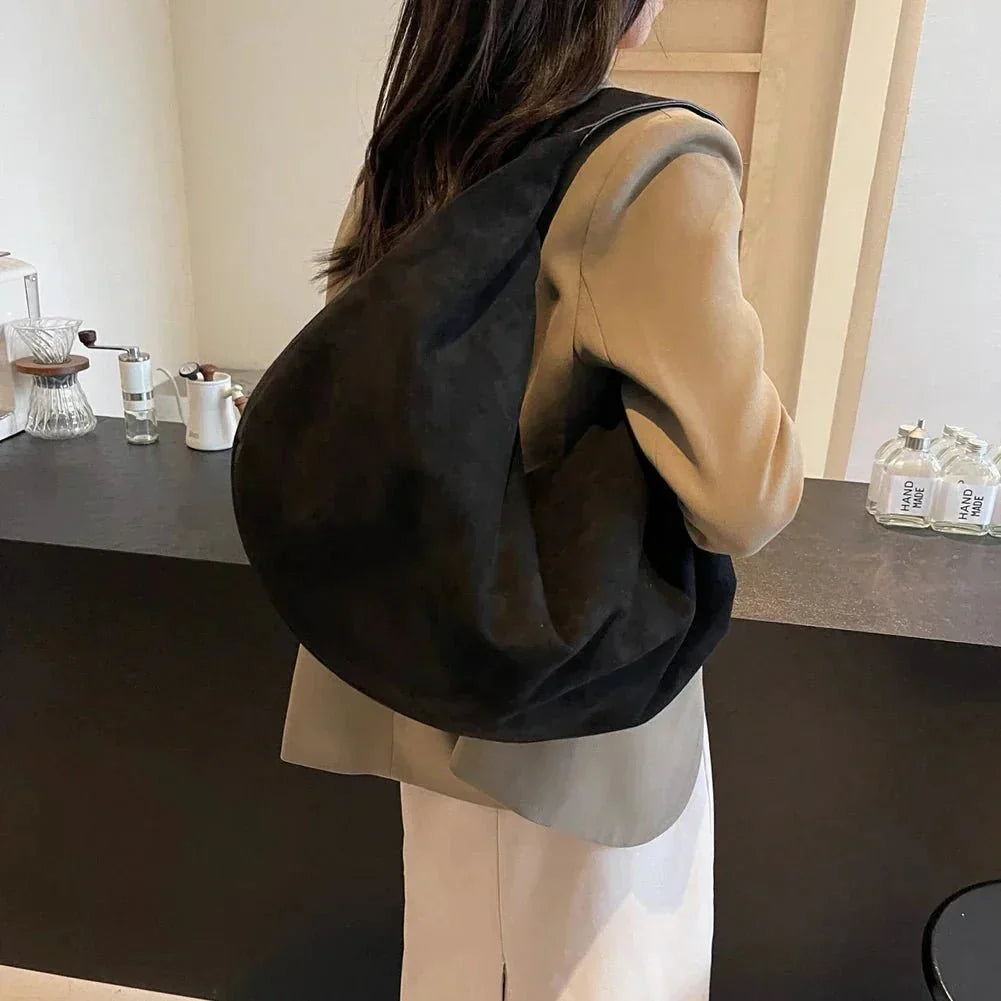 Woman wearing a large black suede hobo handbag with zipper, ideal for work and travel